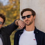 Ein Mann lehnt an einer Säule und trägt die schwarze Leo Sonnenbrille von Hypreader. Die klaren Linien und das matte Schwarz unterstreichen den urbanen Stil.