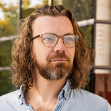 Mann mit lockigem Haar und Bart trägt die Hypreader Blaulichtfilterbrille Lupus in Champagner – moderner Unisex-Stil.