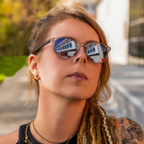 Frau mit Dreadlocks und goldenen Accessoires trägt die Hypreader Lupus Sonnenbrille in Champagner bei einem Streetstyle-Shooting im urbanen Außenbereich.