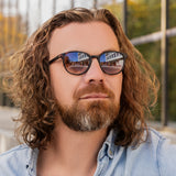 Mann mit längeren Haaren trägt die Sonnenbrille Hypreader Lupus in Havanna  braun – städtische Umgebung spiegelt sich in den Gläsern, entspannter Outdoor-Look.