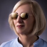 Eine Frau mit blonder Bobfrisur trägt die Phoenix Sonnenbrille Roségold von Hypreader. Die reflektierenden Gläser mit Braunverlauf und die zarte roségoldene Metallfassung ergänzen ihr hellblaues Oberteil harmonisch.