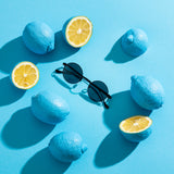 Hypreader Sonnenbrille Vela Schwarz/Grau auf blauem Hintergrund mit gelben Zitronen – stilvolle Flatlay-Szene im Sommer-Look.