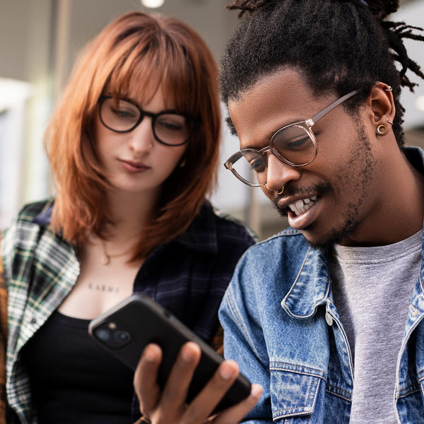 Zwei junge Erwachsene mit Hypreader Blaulichtfilterbrillen Lupus im Gespräch, während sie gemeinsam auf ein Smartphone schauen – modernes Design, ideal für Bildschirmarbeit und digitalen Alltag