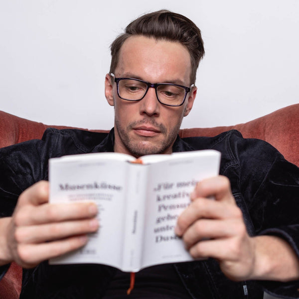 Person mit Blaulichtfilterbrille liest ein Buch – stilvoller Augenschutz beim Lesen