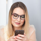 Frau mit blonden Haaren trägt die Hypreader Aries Brille in Blau beim Blick aufs Smartphone – ideal für Bildschirmarbeit.