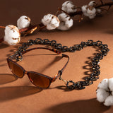 Lifestyle-Aufnahme der Hypreader Brillenkette in Braun-Gold mit Sonnenbrille  Pyxis von Hypreader – Dekoration mit Baumwollzweigen, stilvoll in Szene gesetzt.