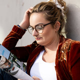 Frau mit Hypreader Lupus Blaulichtfilterlesebrille in Champagner beim Lesen einer Zeitschrift, natürliches Licht und entspannter Moment.