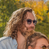 Bei herbstlicher Sonne zeigt dieses Bild einen Mann mit langen Locken, der die Orion Sonnenbrille von Hypreader in Grau Transparent trägt.
