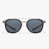 Frontalansicht der transparent-grauen Hypreader-Fassung mit aufgesetztem Orion Sonnenclip. Die Gläser sind gleichmäßig grau getönt. Die obere Brücke aus Metall verläuft parallel zur Kunststoffbrücke darunter.