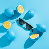 Hypreader Aries Sunclip Sonnenbrille im stylischen Setting – schwarzes Gestell mit grünem Clip, präsentiert auf blauem Hintergrund mit Zitronen.