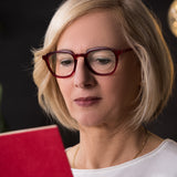 Frau mit blonder Bobfrisur trägt die Hypreader Brille Orion in Rot beim Lesen eines roten Buches – Modelbild mit Fokus auf Blaulichtfilter für Bildschirm- und Lesearbeit.