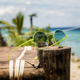 Hypreader Vela Gelb Sonnenbrille mit runden Gläsern in blauer Verlaufstönung auf einem Holzpfosten am tropischen Strand