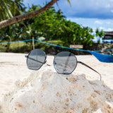 Hypreader Libra Schwarz – Sonnenbrille mit dunkelgrauen Gläsern am Strand auf weißem Stein.