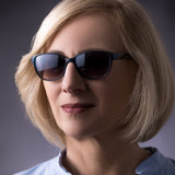 Eine Frau mittleren Alters präsentiert die Pyxis Sonnenbrille von Hypreader in Petrol. Die getönten Verlaufsgläser passen sich harmonisch dem Gesicht an und sorgen für einen eleganten Look mit optimalem UV-Schutz.